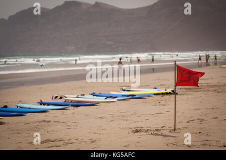 Bandiera rossa lembo sulla spiaggia, tavole da surf in background Foto Stock