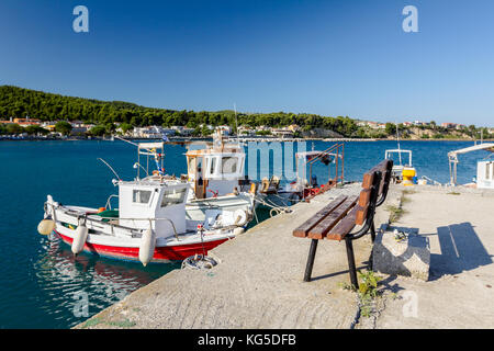 Panca in legno è rivolta verso le piccole barche da pesca con attrezzi legati con funi per il molo, wharf. marina. Foto Stock