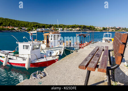 Panca in legno è rivolta verso le piccole barche da pesca con attrezzi legati con funi per il molo, wharf. marina. Foto Stock