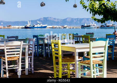 Sedie e tavoli in outdoor tipica taverna greca nella luce del sole di mattina con ombre vicino al molo. Foto Stock