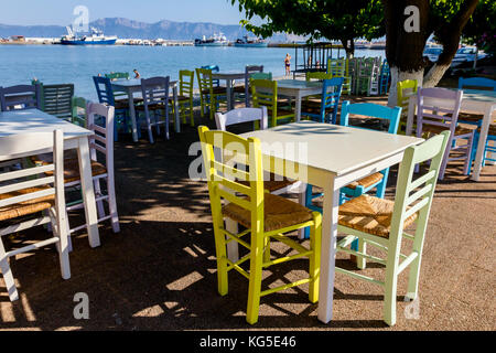 Sedie e tavoli in outdoor tipica taverna greca nella luce del sole di mattina con ombre vicino al molo. Foto Stock