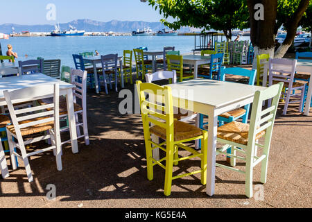 Sedie e tavoli in outdoor tipica taverna greca nella luce del sole di mattina con ombre vicino al molo. Foto Stock