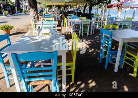 Sedie e tavoli in outdoor tipica taverna greca nella luce del sole di mattina con ombre vicino al molo. Foto Stock