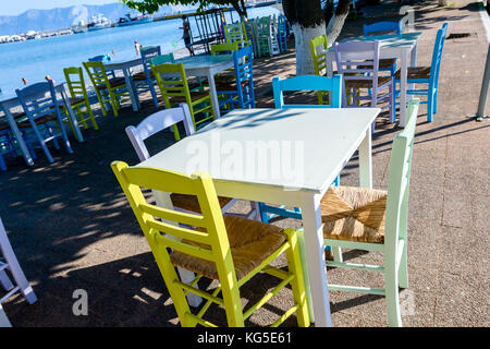 Sedie e tavoli in outdoor tipica taverna greca nella luce del sole di mattina con ombre vicino al molo. Foto Stock