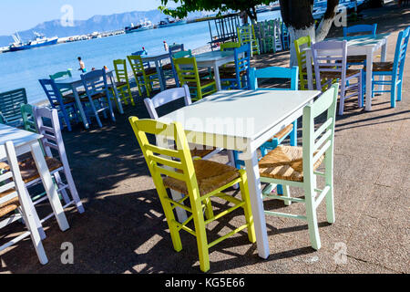 Sedie e tavoli in outdoor tipica taverna greca nella luce del sole di mattina con ombre vicino al molo. Foto Stock