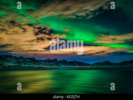 Aurora boreale sopra il lago kleifarvatn, Islanda. nuvoloso in serata con luci del nord riflettendo sul lago. Foto Stock