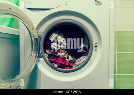 Una chiusura di una macchina di lavaggio caricata con vestiti isolati su sfondo bianco. il bucato in lavatrice con la porta aperta. Foto Stock