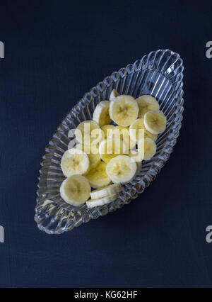 Fette di banana in recipiente di vetro su sfondo nero - vista superiore fotografia Foto Stock