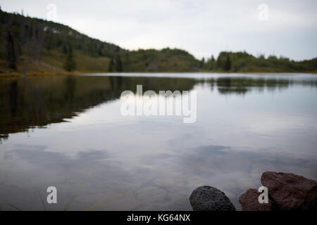 Tranquillo tranquillo lago in un cupo giorno nuvoloso con le nuvole grigie e il bosco circostante sulle colline si riflette nell'acqua Foto Stock