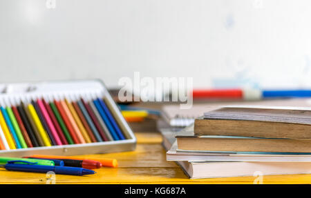 Matite colorate, penne e chiuso i libri e quaderni sulla parte superiore di un giallo tavolo in legno con una scuola di bianco scheda in background Foto Stock