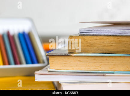 Matite colorate, penne e chiuso i libri e quaderni sulla parte superiore di un giallo tavolo in legno con una scuola di bianco scheda in background Foto Stock