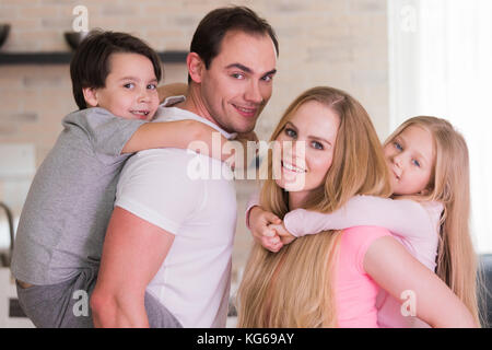 Ritratto di famiglia felice, padre e madre dando un ragazzo e una ragazza piggy back ride a casa Foto Stock