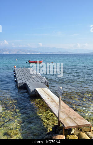 Un vecchio molo o pontile con una barca ancorata nel mare mediterraneo alla fine. acque cristalline e il blu del mar Ionio e del cielo. Foto Stock