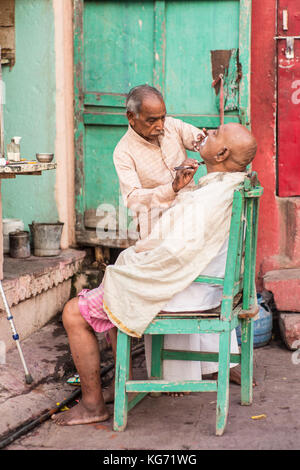 Rasatura barbiere un uomo per le strade di Varanasi (India). Foto Stock