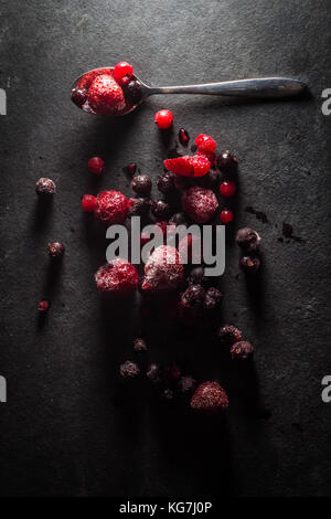 Misto di frutti di bosco selvatici sat su un livello di grigio ardesia piatto di portata spolverati di zucchero con un cucchiaio di lucido Foto Stock