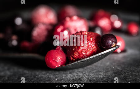 Misto di frutti di bosco selvatici sat su un livello di grigio ardesia piatto di portata spolverati di zucchero con un cucchiaio di lucido Foto Stock