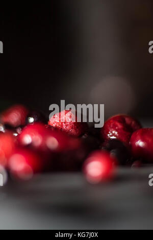 Misto di frutti di bosco selvatici sat su un livello di grigio ardesia piatto di portata spolverati di zucchero con un cucchiaio di lucido Foto Stock