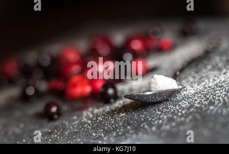 Misto di frutti di bosco selvatici sat su un livello di grigio ardesia piatto di portata spolverati di zucchero con un cucchiaio di lucido Foto Stock