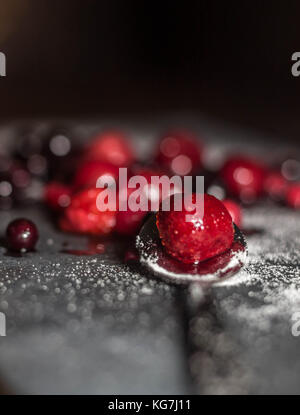 Misto di frutti di bosco selvatici sat su un livello di grigio ardesia piatto di portata spolverati di zucchero con un cucchiaio di lucido Foto Stock