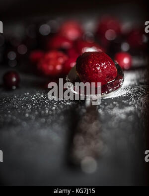 Misto di frutti di bosco selvatici sat su un livello di grigio ardesia piatto di portata spolverati di zucchero con un cucchiaio di lucido Foto Stock