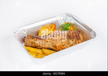 Chiudere fino sano ristorante Consegna del cibo in scatola di lamina. grigliate di carne bistecca e Spicchi di patate. I pasti da asporto, il fuoco selettivo. isolato sul bianco b Foto Stock