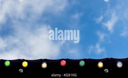 Happy Holiday, evento celebrazione il concetto di sfondo: linea di coloratissimi lampadine sulla gronda del tetto guardando in alto, cielo blu e nuvole bianche in backgroun Foto Stock