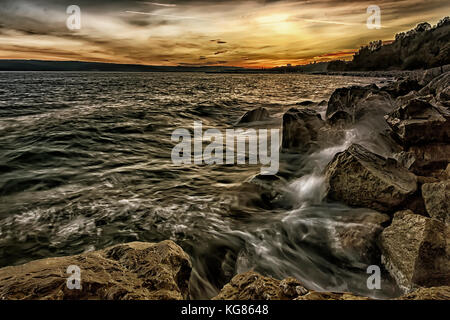 Tramonto sul mare con onde splash sulle rocce Foto Stock