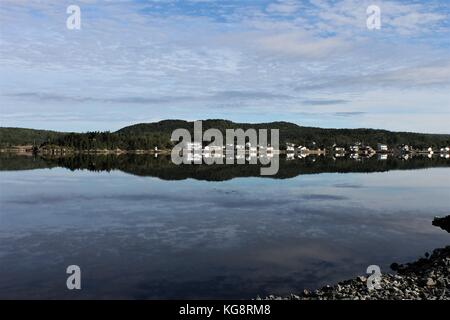 Guardando attraverso il porto con le case e gli edifici lungo il litorale si riflette nell'acqua calma, la mattina presto, Eastport, Terranova Labrador. Foto Stock