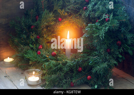 Una ghirlanda di Natale fatto di rami di abete, ginepro, tuja, bosso e rosa selvatica bacche. corona con candele accese. Foto Stock