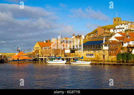 Porto di Whitby con la stazione di bagnanti, due barche a vela ormeggiate e la chiesa di Santa Maria in autunno luce del sole Foto Stock