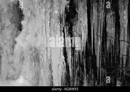 Ghiaccioli appesi al lato di una scogliera rocciosa. immagine in bianco e nero Foto Stock