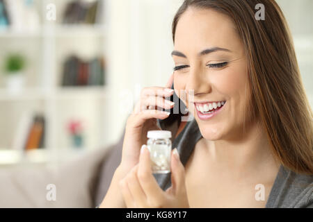 Felice paziente chiedendo informazioni sul telefono cellulare di circa pillole seduto su un divano in un interno di una casa Foto Stock