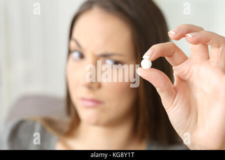 Donna sospetti guardando un tondo bianco pillola seduto su un divano in un interno di una casa Foto Stock