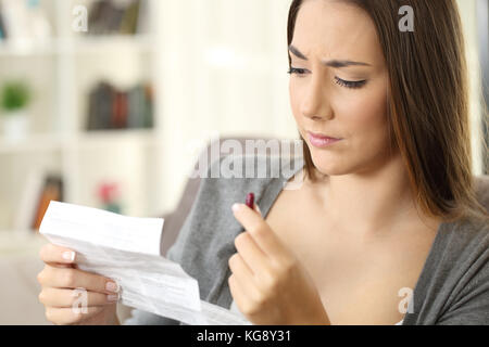 La donna la lettura di un foglio illustrativo prima di prendere una pillola rossa seduta su un divano nel soggiorno in un interno di una casa Foto Stock