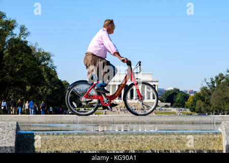 Ciclista maschile in sella a una bicicletta Capital Bikeshare, Abraham Lincoln Memorial in the background, Washington, DC, Stati Uniti d'America, USA. Foto Stock