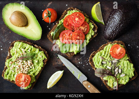 Verde sano veggie toast con avocado, pomodoro, germogli e semi sul buio backgrop. tabella vista dall'alto. cibo sano, dieta vegana concept Foto Stock