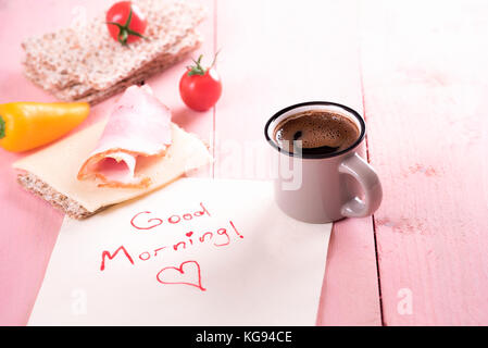 Semplice pasto sano con tutta di pani croccanti di grano, pomodori, formaggi, carne e una tazza di caffè, su un tovagliolo con un buon mattino messaggio, al mattino Foto Stock