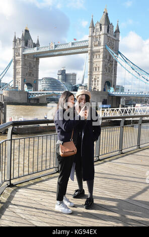 I turisti scattano foto al Tower Bridge, poiché il freddo ma luminoso clima autunnale attrae turisti e londinesi per esplorare le attrazioni del centro di Londra. Foto Stock