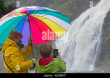 Ragazzo prendendo foto di al Powerscourt Waterfall, madre holding ombrello, Enniskerry, Co. Wicklow, Irlanda Foto Stock
