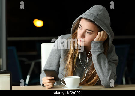 Triste pensieroso adolescente ascoltare musica in un bar di notte e guardando a lato Foto Stock