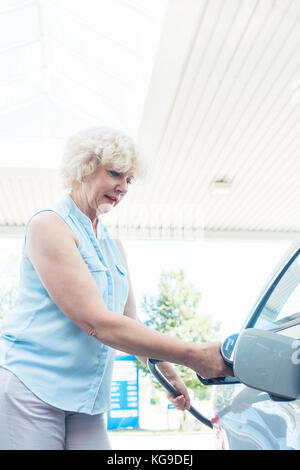 Active senior donna sorridente mentre si riempie il serbatoio del gas della sua Foto Stock