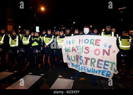 Londra, Regno Unito. 5 novembre 2017. Cordone di polizia sulla strada durante la "maschera illion marzo " manifestazione organizzata da anonimo ispirato attivisti. Un manifestante indossa anonimo V per Vendetta maschera è in possesso di un cartellone di lettura: 'Non più morti sulle nostre strade. #Opsafewinter'. Credito: ZEN - Zaneta Razaite / Alamy Live News Foto Stock