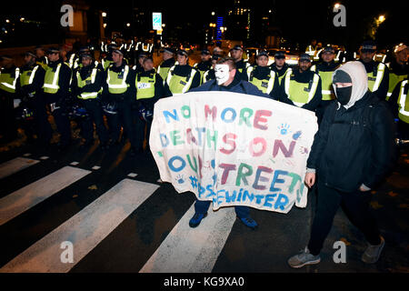 Londra, Regno Unito. 5 novembre 2017. Cordone di polizia sulla strada durante la "maschera illion marzo " manifestazione organizzata da anonimo ispirato attivisti. Un manifestante indossa anonimo V per Vendetta maschera è in possesso di un cartellone di lettura: 'Non più morti sulle nostre strade. #Opsafewinter'. Credito: ZEN - Zaneta Razaite / Alamy Live News Foto Stock