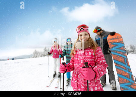Ragazza sorridente con la famiglia sul terreno di sci pronti per lo sci Foto Stock