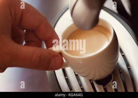 Vista ravvicinata della mano di un uomo che lavora in una casa di caffè la preparazione di caffè espresso in attesa per la macchina da caffè per terminare versando la beve fresco Foto Stock