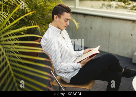 Uomo seduto sulla biblioteca e leggere il libro con la sfocatura sullo sfondo Foto Stock