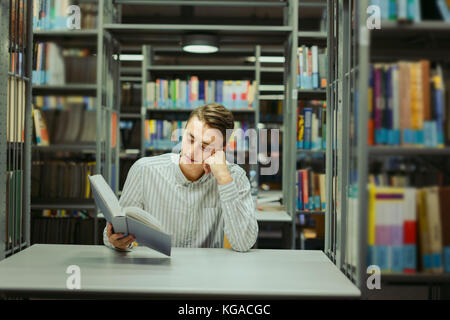 Uomo seduto sulla biblioteca e leggere il libro con la sfocatura sullo sfondo Foto Stock