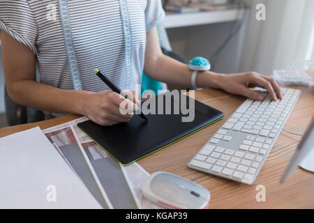 La sezione centrale del designer femmina con tavoletta grafica al banco in casa Foto Stock
