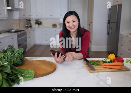 Ritratto di donna sorridente con tavoletta digitale in cucina Foto Stock