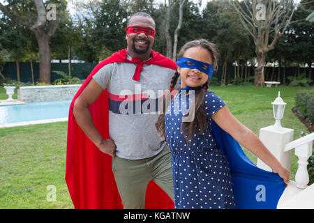 Ritratto di Padre sorridente e la figlia in costume da supereroe in piedi in giardino Foto Stock